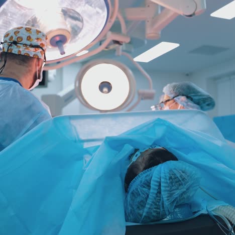 patient is lying on a surgical table in clinic. professional doctors doing a plastic surgery under the bright light in the operating theatre.
