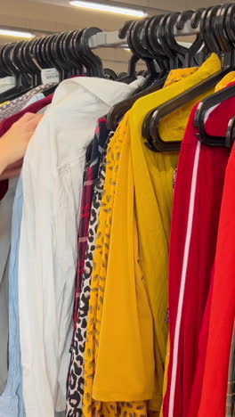 young woman selecting fuchsia sweater in dressing room, carefully examining sleeve length, checking appearance in mirror while making expressive gestures. concept of buying women clothes