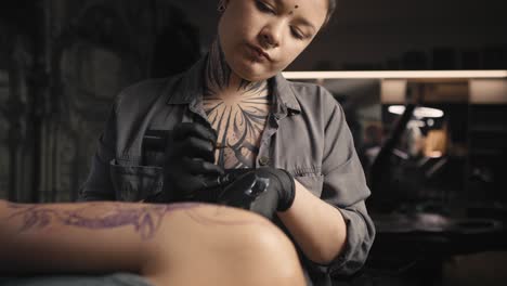 foco en una mujer caucásica tatuando los brazos de su cliente.