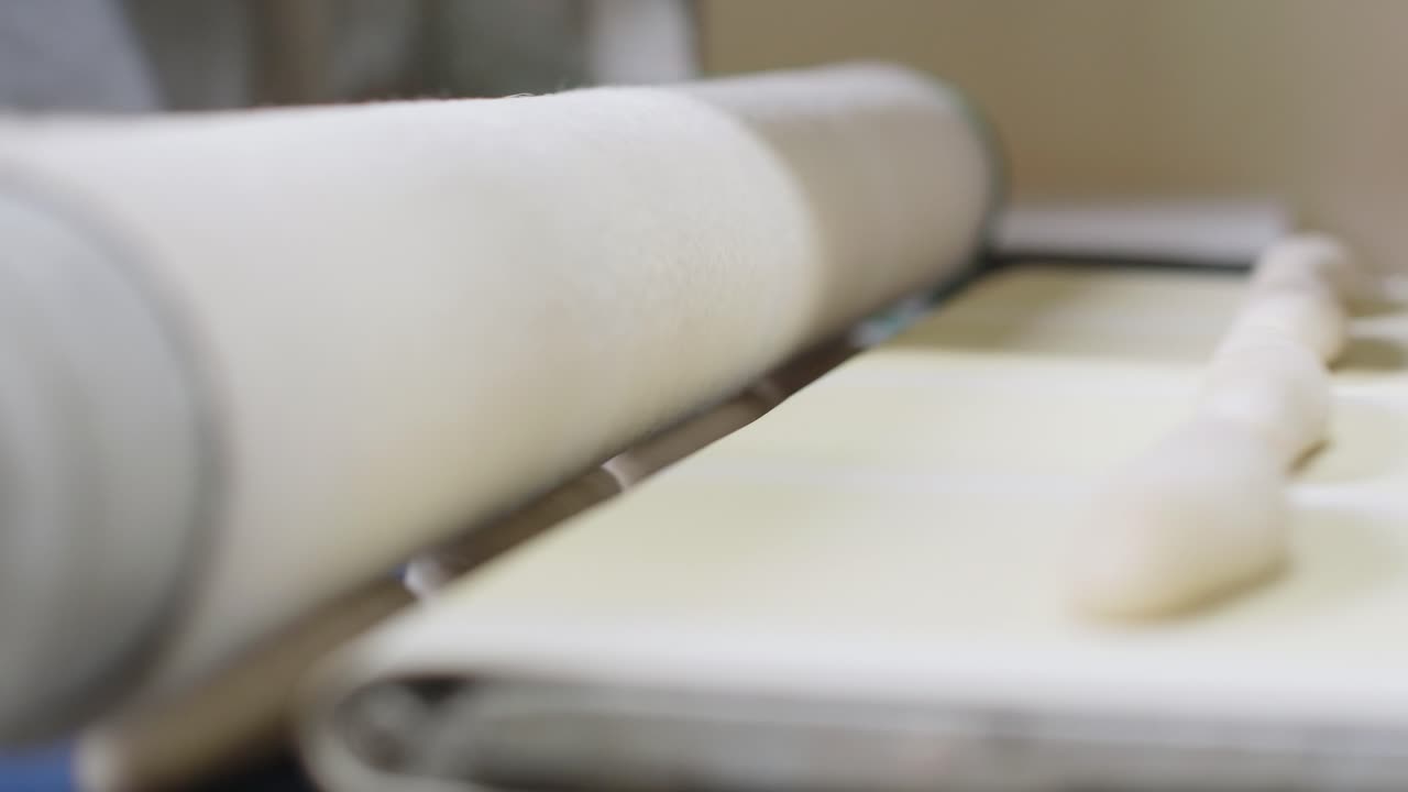Fresh Bread Dough Moving On Conveyor Belt And Being Pressed By Roller. Low Angle, Close Up