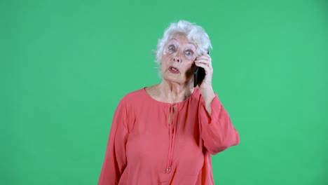 retrato de una mujer mayor mirando a la cámara y hablando en su teléfono inteligente. abuela de cabello gris en blusa roja en pantalla verde en el estudio. cerca