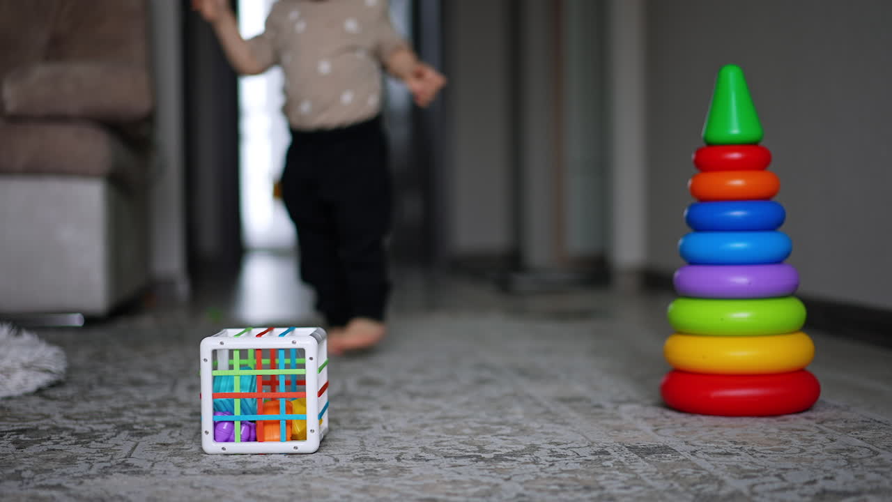 Little boy runs along the room approaching camera. Child goes past toys lying on the floor.