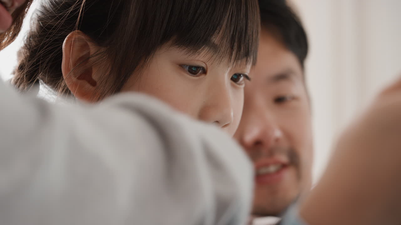 태블릿 컴퓨터를 사용하는 작은 아시아 소녀 부모와 함께 엔터테인먼트를 시청하고 터치 스크린 장치에서 게임을하고 온라인 브라우징을하고 집에서 소파에서 함께 휴식을 취합니다 4k