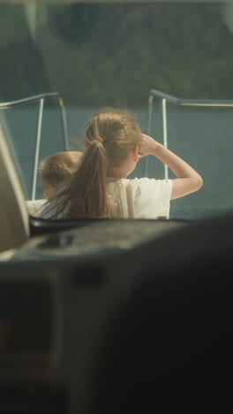 little girl and junior brother sit on sailboat bow deck view from skipper cockpit. cute children observe seascape sailing yacht on summer vacation