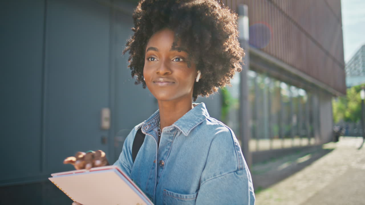 Young woman student walking outdoors with notebooks