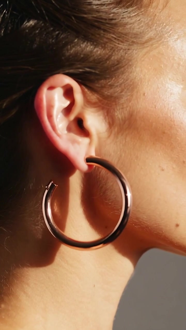 Video verticale: Donna che si gira sul lato destro, capelli raccolti all'indietro, un orecchino a cerchio che oscilla per rivelare la chiusura sul set.