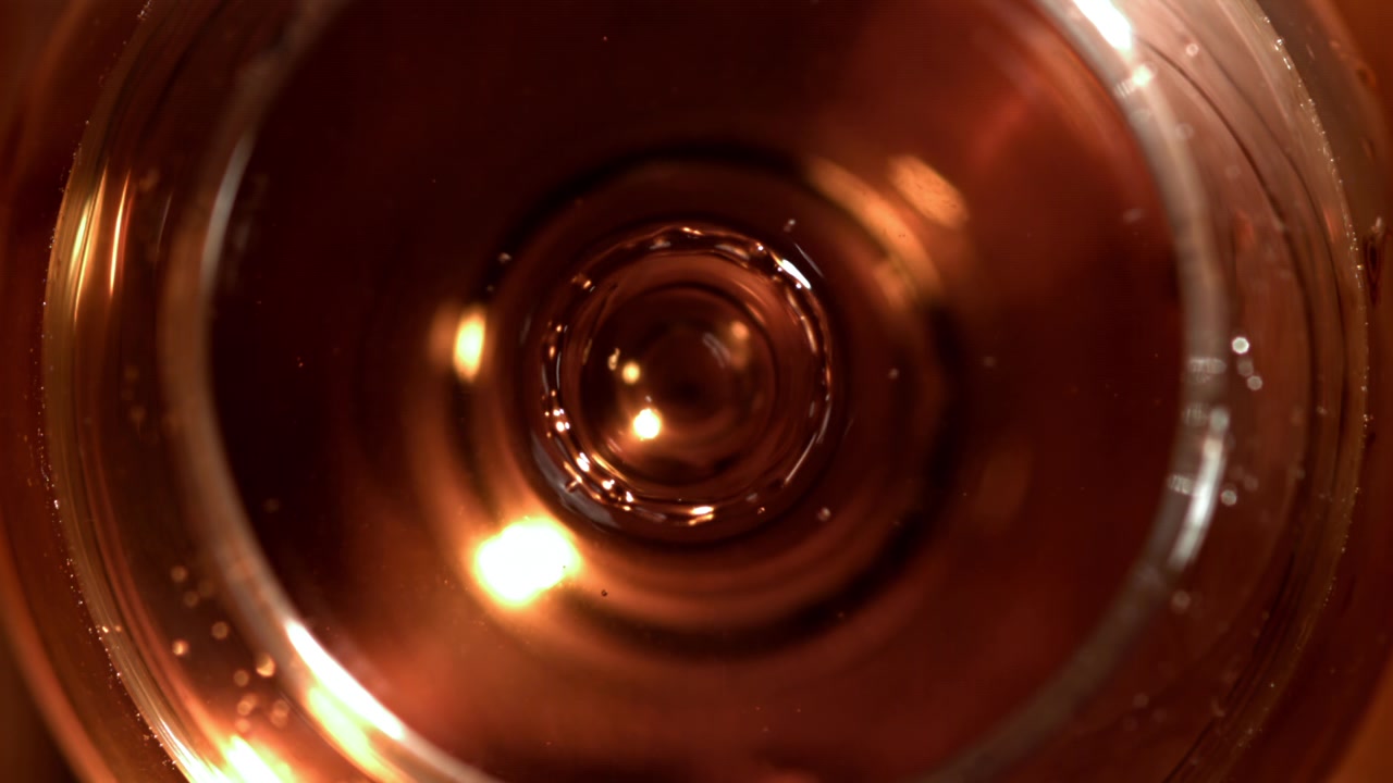 Goccia che schizza in un liquido ambrato in un bicchiere al rallentatore