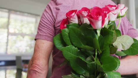 hombre mayor caucásico dando un ramo de flores a su esposa en casa