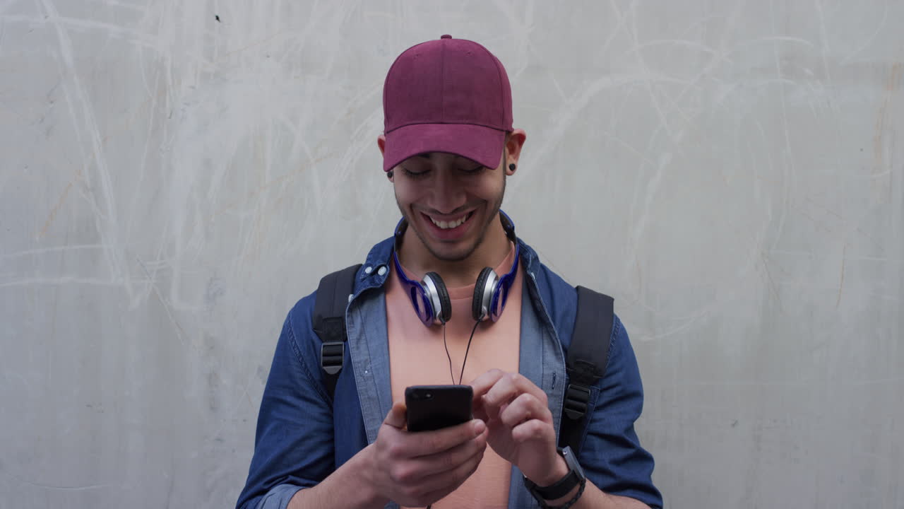 retrato de un joven estudiante hispano que usa un teléfono inteligente disfrutando de navegar por mensajes de texto en las redes sociales en una aplicación de comunicación de teléfono móvil sonriendo alegremente