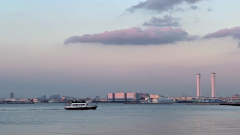 Fähre-überquert-Ruhige-Gewässer-Mit-Skyline-Der-Stadt-In-Der-Abenddämmerung,-Heitere-Abendstimmung,-Weitwinkelaufnahme