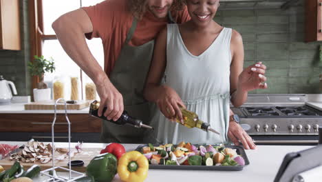 una pareja diversa, un joven caucásico y una mujer afroamericana, cocinando juntos en casa.