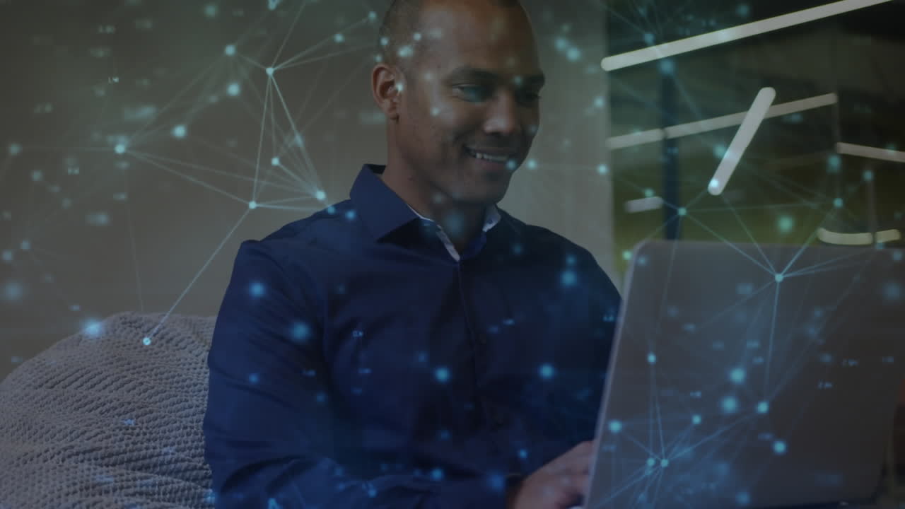 Animation of communication network over smiling biracial man using laptop in office