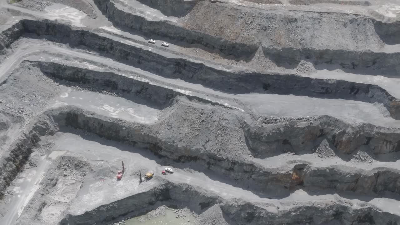 Aerial view of a stepped quarry featuring striking turquoise water pools and visible excavation layers.