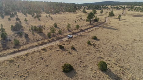 Wide-aerial-as-overlanding-vehicle-travels-down-remote-desert-dirt-road,-4K