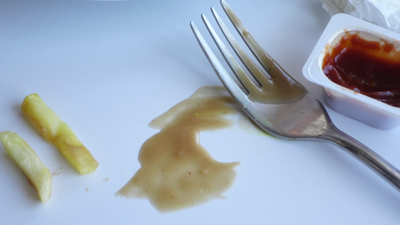 Piatto sporco con patatine fritte, una forchetta sporca e avanzi di salsa.