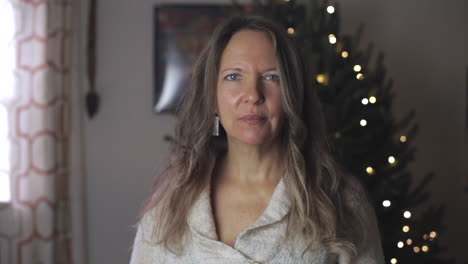 portrait of a woman in her 50s looking seriously at the camera while standing in the house with christmas tree in background