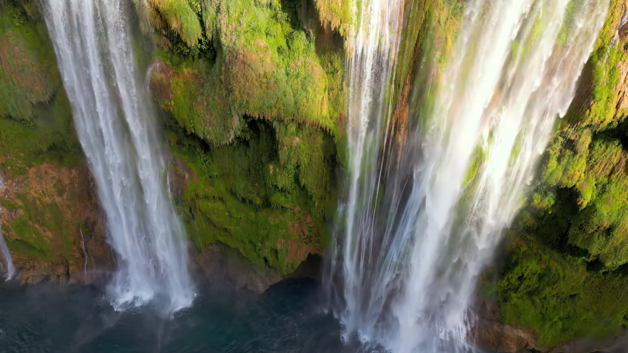 Aerial drone view of Tamul Waterfall cascading down green cliffs into a turquoise pool below
