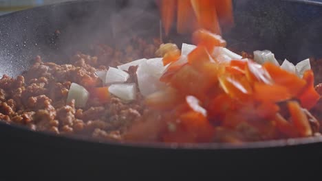 Adding-Chopped-White-Onion,-Red-Bell-Pepper,-And-Salt-Into-Ground-Turkey-Meat-Cooking-In-Pan