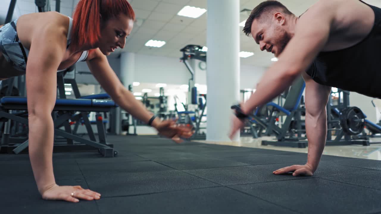 Couple doing push ups. Young motivated aggressive attractive focused sporty active couple doing push ups and holding hands together while looking each other in the modern gym
