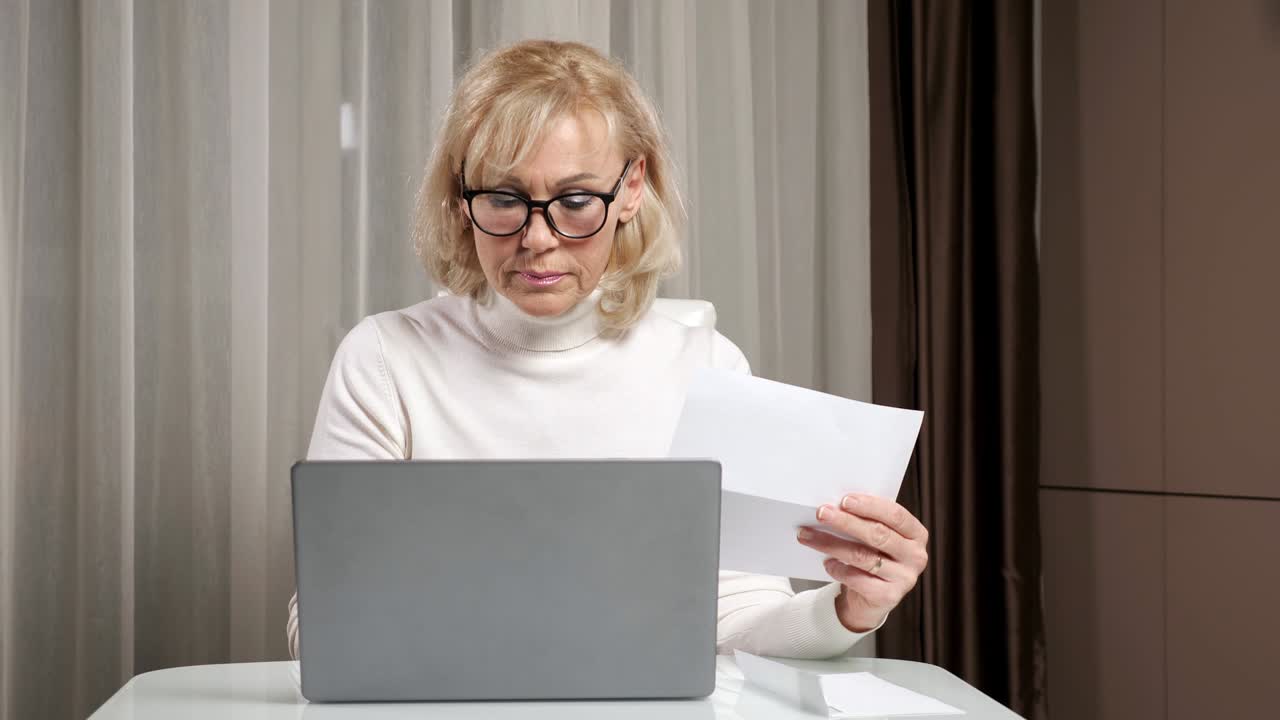Donna matura apre una busta, scrive e conta le bollette delle utenze.