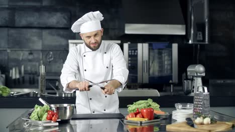 Male-chef-posing-at-professional-kitchen.-Cook-playing-with-sharpening-knives