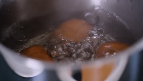 close up of brown eggs inside a pot of boiling water on a stovetop