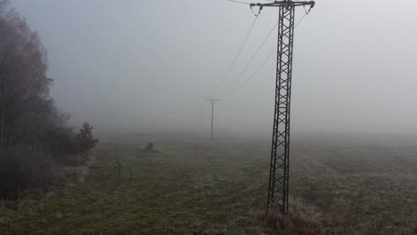 aerial view of electricity towers and dense fog in agricultural field on autumn morning, pedestal drone shot