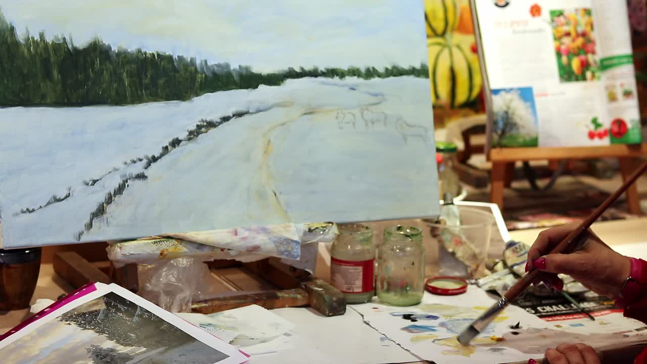 나이든 여자가 겨울 그림에 색을 더하고 페인트를 섞고 있다