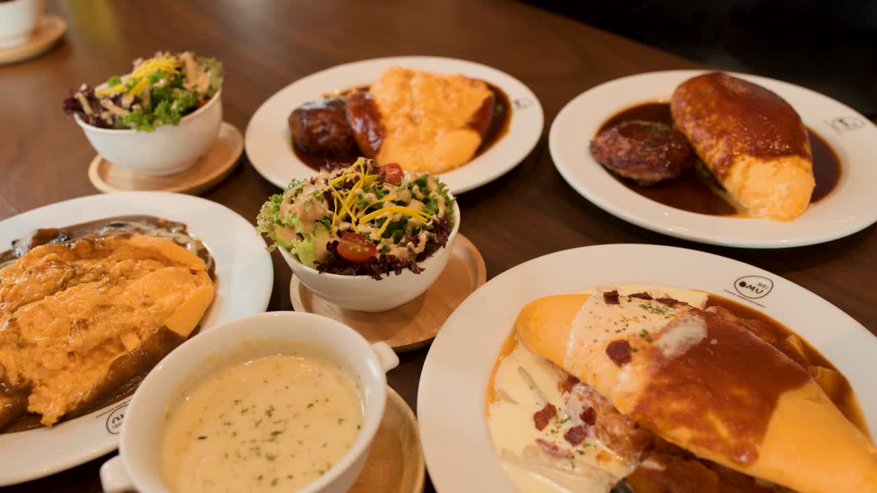 Overhead view of Japanese omelette rice, creamy soup, salad, and bread in warm restaurant lighting