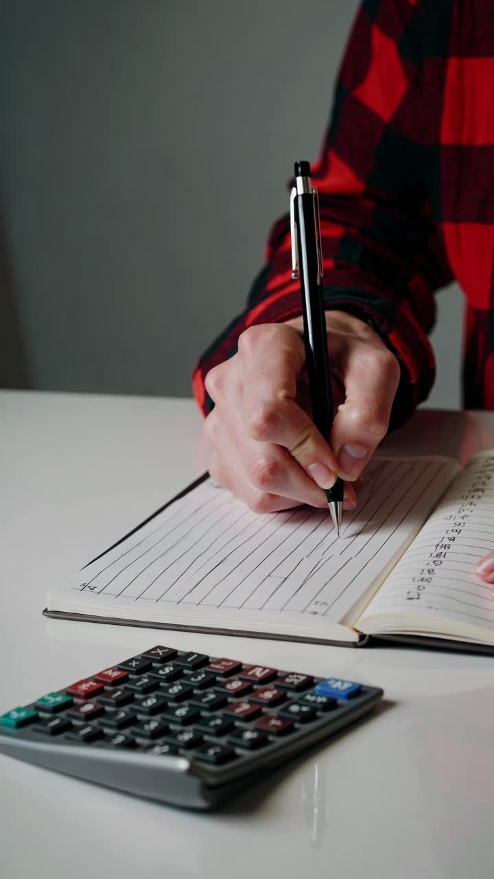 Close-up video shot of a person writing in a notebook with a pen, a calculator nearby
