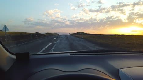 view from inside car on empty hilly road leading to horizon line at sunset or sunrise