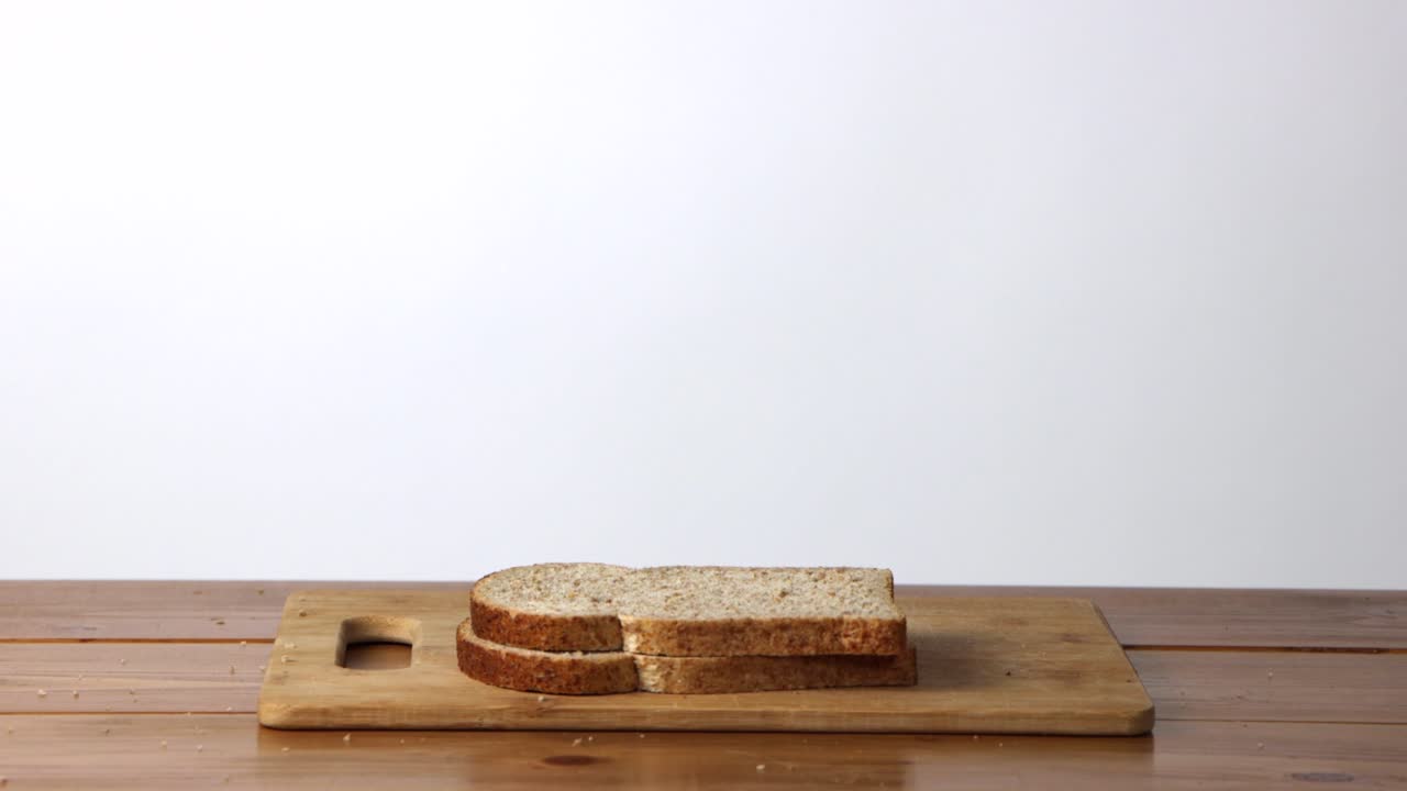 통밀 빵 조각이 흰색 배경에 있는 나무 커팅 보드에 한 번에 하나씩 떨어지는
