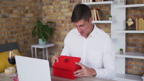 caucasian man making video call using laptop opening gift box and talking