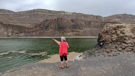 senior, female pointing to the cliffs surrounding alkali lake in northern washington state on a cloudy, breezy afternoon