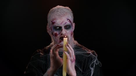 man with halloween zombie bloody wounded makeup, trying to scare, spells conjures over a candle