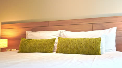 slow tilt-down on the made-up clean bed in a modern hotel in thailand with green and white pillows and lamp light on a side