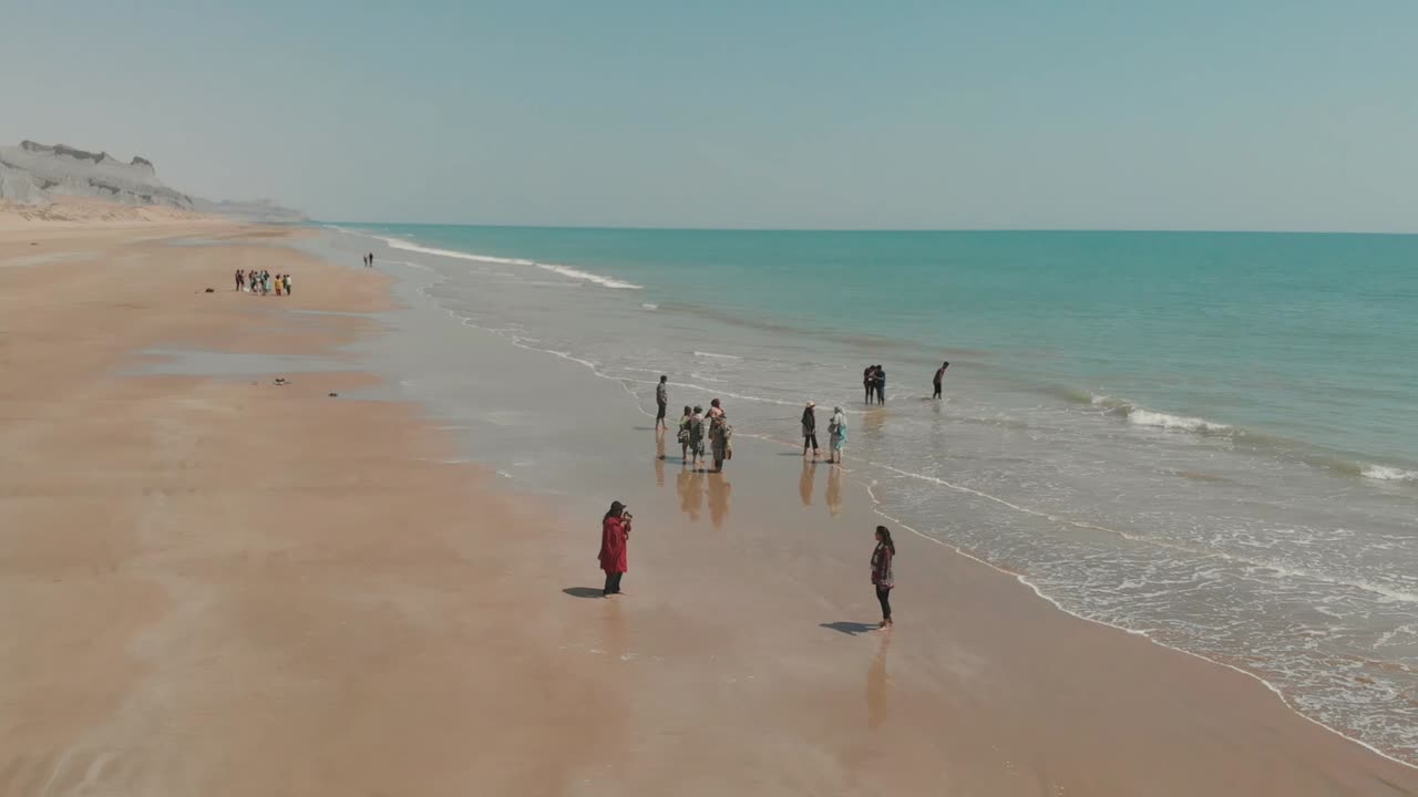 People Enjoying Wading In Water On Golden Beach In Balochistan. Aerial Follow Shot