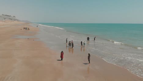 people enjoying wading in water on golden beach in balochistan. aerial follow shot
