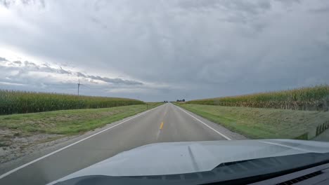pov conduciendo en una carretera rural pasando por turbinas eólicas y campos en un día nublado a finales del verano en el medio oeste