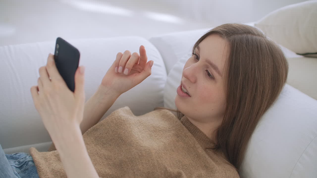 현대적인 인테리어와 함께 거실에 앉아서 스마트폰으로 이야기하는 성숙한 여성. 기술과 휴식의 개념.