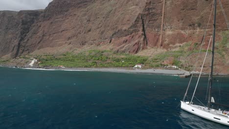 Sailing-boat-anchored-in-blue-water-surrounding-Madeira-island,-aerial