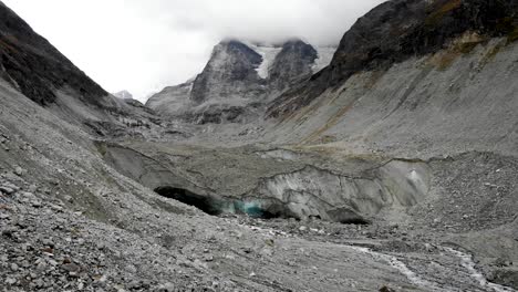 aerial flyover towards the end of the zinal glacier in valais, switzerland with a view of the melting glacial water stream and the alpine valley