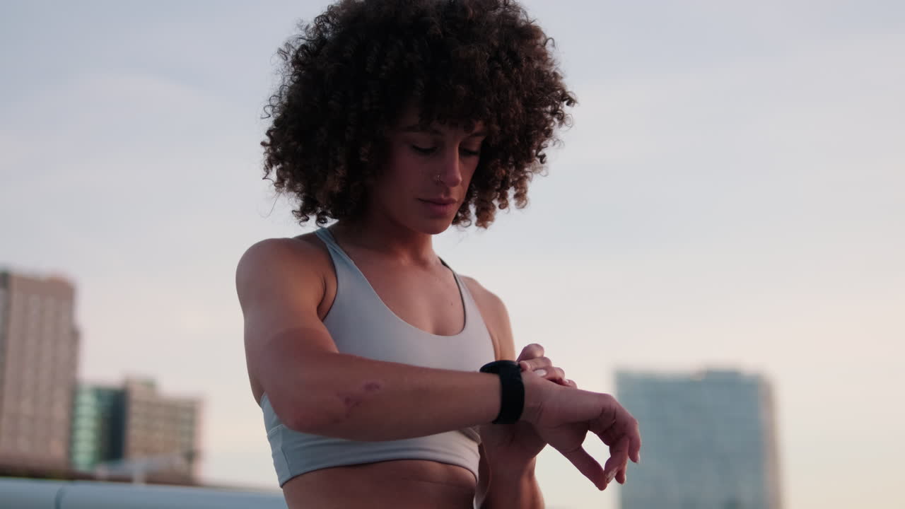 Woman Checks Fitness Tracker on Rooftop at Sunset