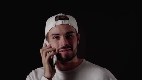 trendy 20s man answering mobile phone excited, close, black background