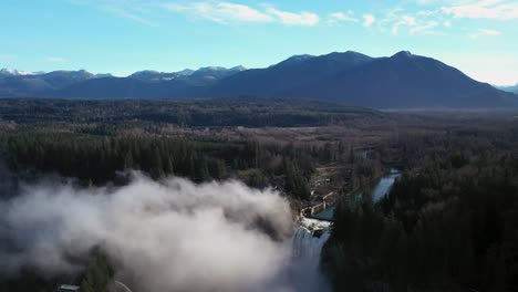 toma aérea hacia atrás de las hermosas cataratas de snoqualmie escondidas por una manta de niebla y una clara toma amplia del bosque y las montañas en el fondo
