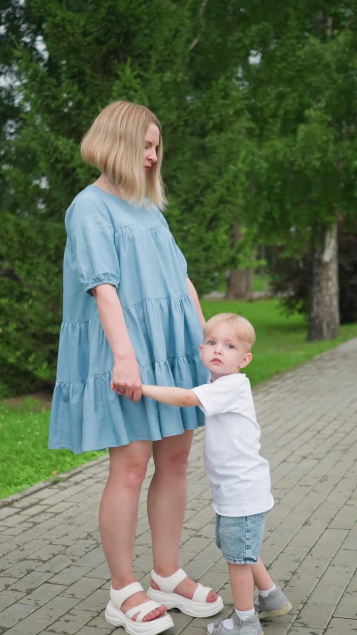 un tierno momento entre una madre y su hijo tomados de la mano mientras están de pie en una pasarela pavimentada rodeada de un exuberante parque verde