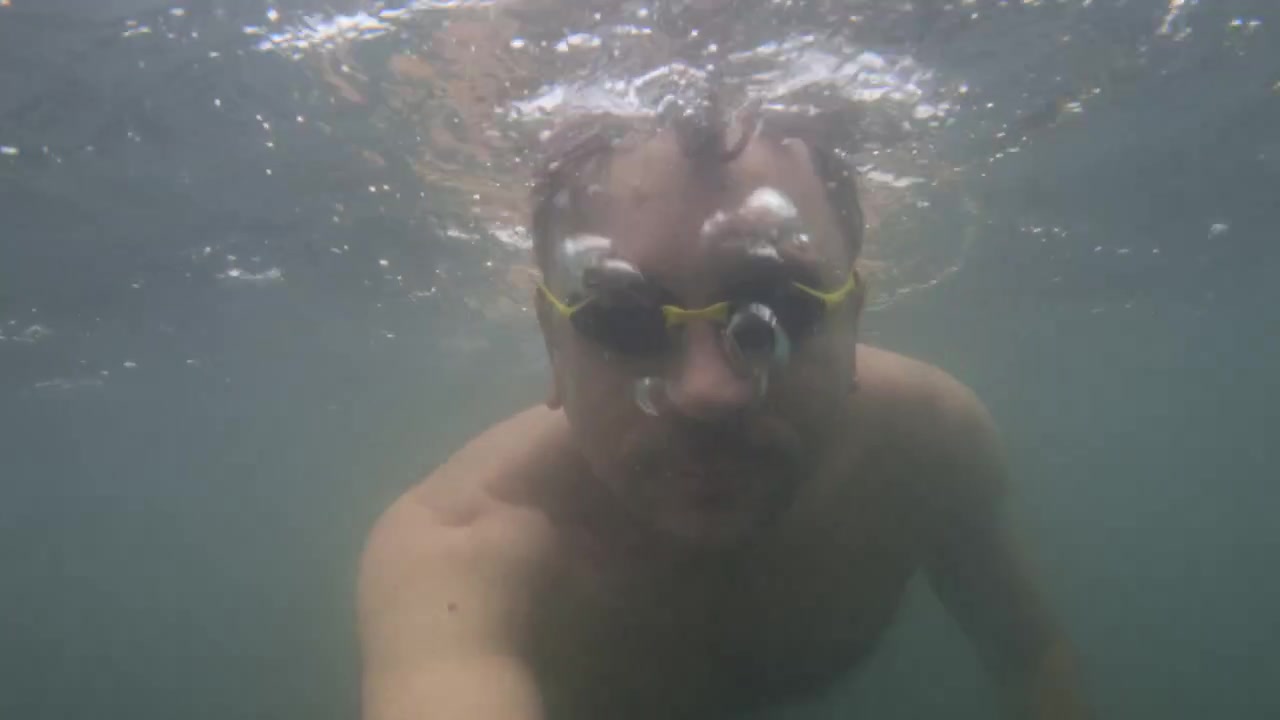 Man in swimming goggles emerging from water, surrounded by air bubbles, enjoying a refreshing swim during an outdoor summer activity