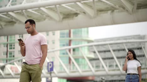 Focused-young-man-walking-on-street-and-looking-at-phone