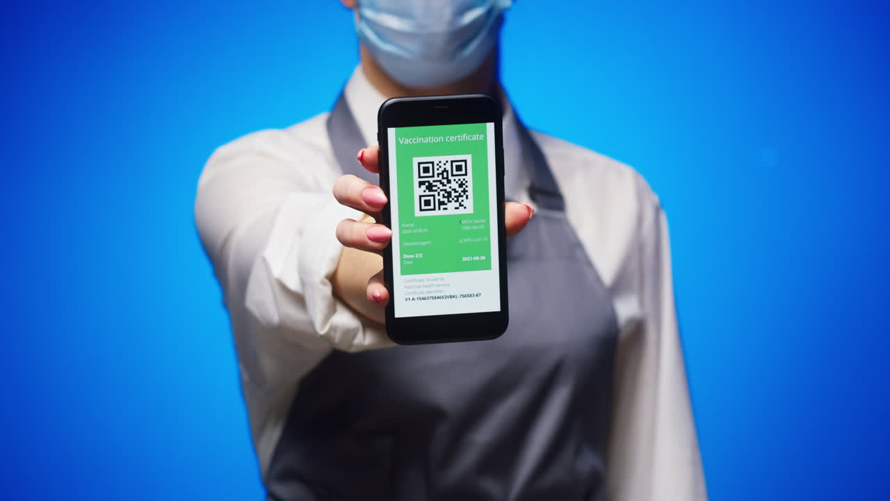 Person in Mask and Apron Showing Digital Vaccination Certificate on Smartphone