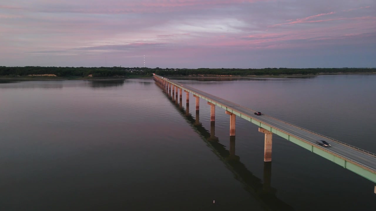 Riprese aeree con drone della passerella pedonale Mile Long Bridge che si estende sul lago Saylorville vicino a Des Moines, Iowa, al tramonto con il cielo rosa riflesso nell'acqua calma